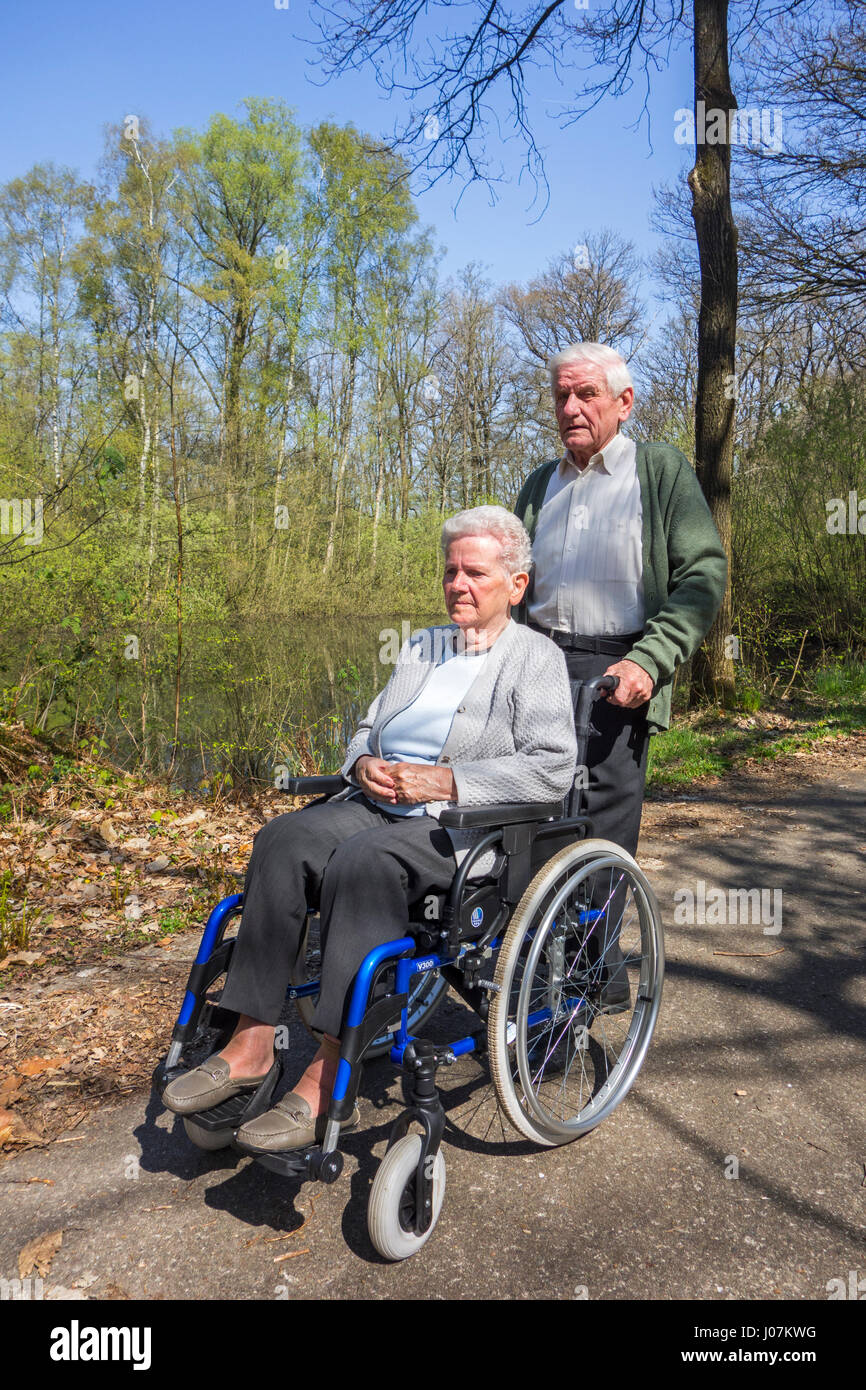 Retired husband taking disabled elderly wife in wheelchair for a walk