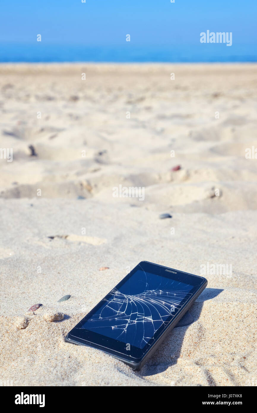 Close up picture of a mobile phone with broken screen in sand on a beach, selective focus. Stock Photo