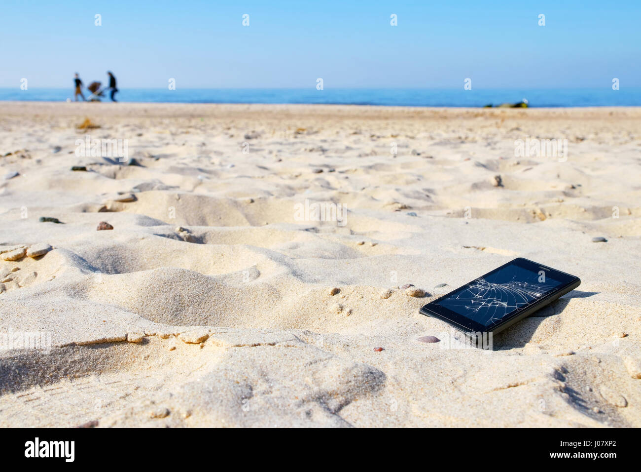 Mobile phone with broken screen in sand on a beach, selective focus. Stock Photo