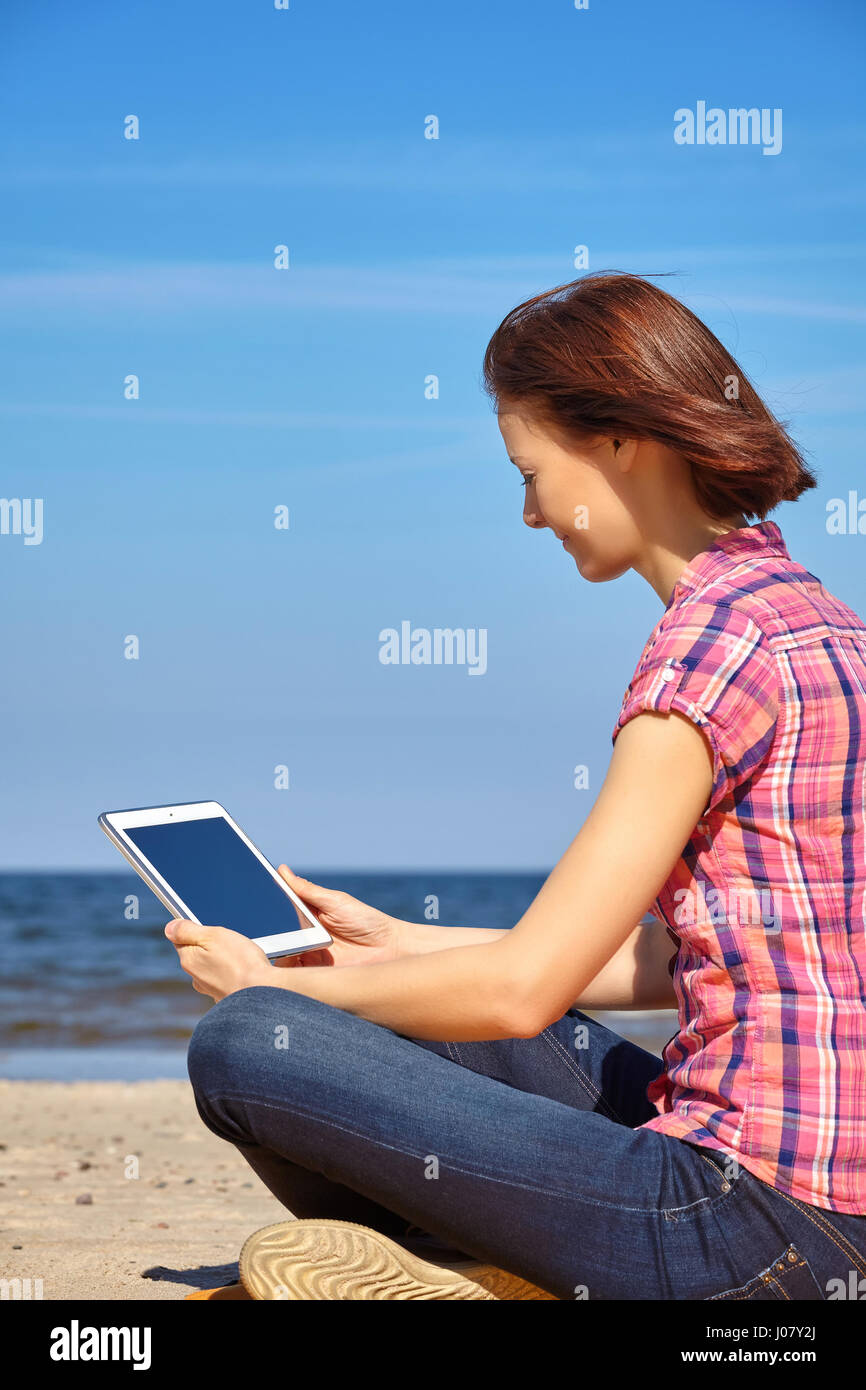Young woman uses tablet computer on a beach, blank screen with copy space. Stock Photo