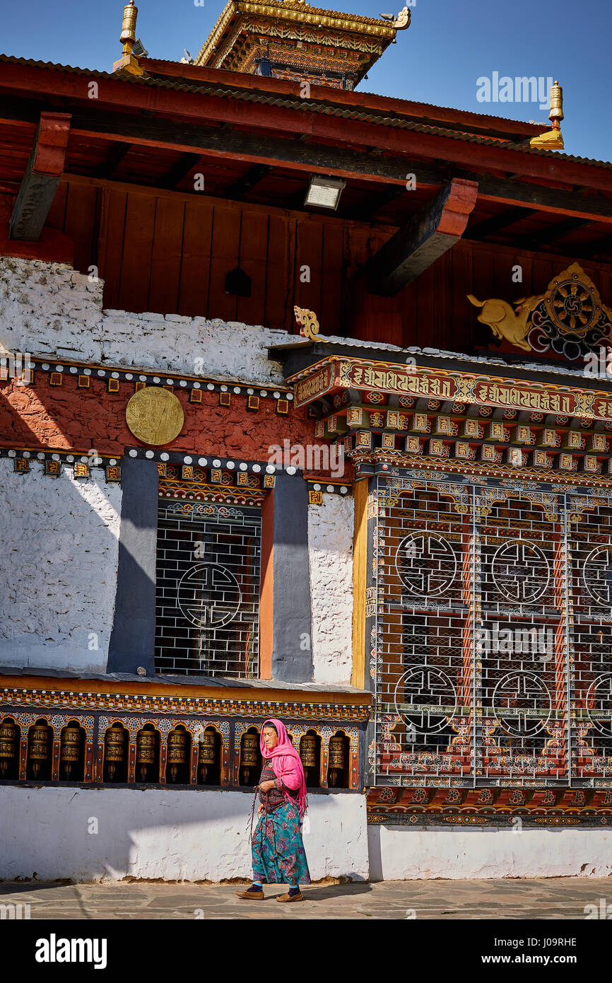 A woman walks past the prayer wheels on the wall of the Changangkha Lhakhang Temple in Thimphu Bhutan Stock Photo