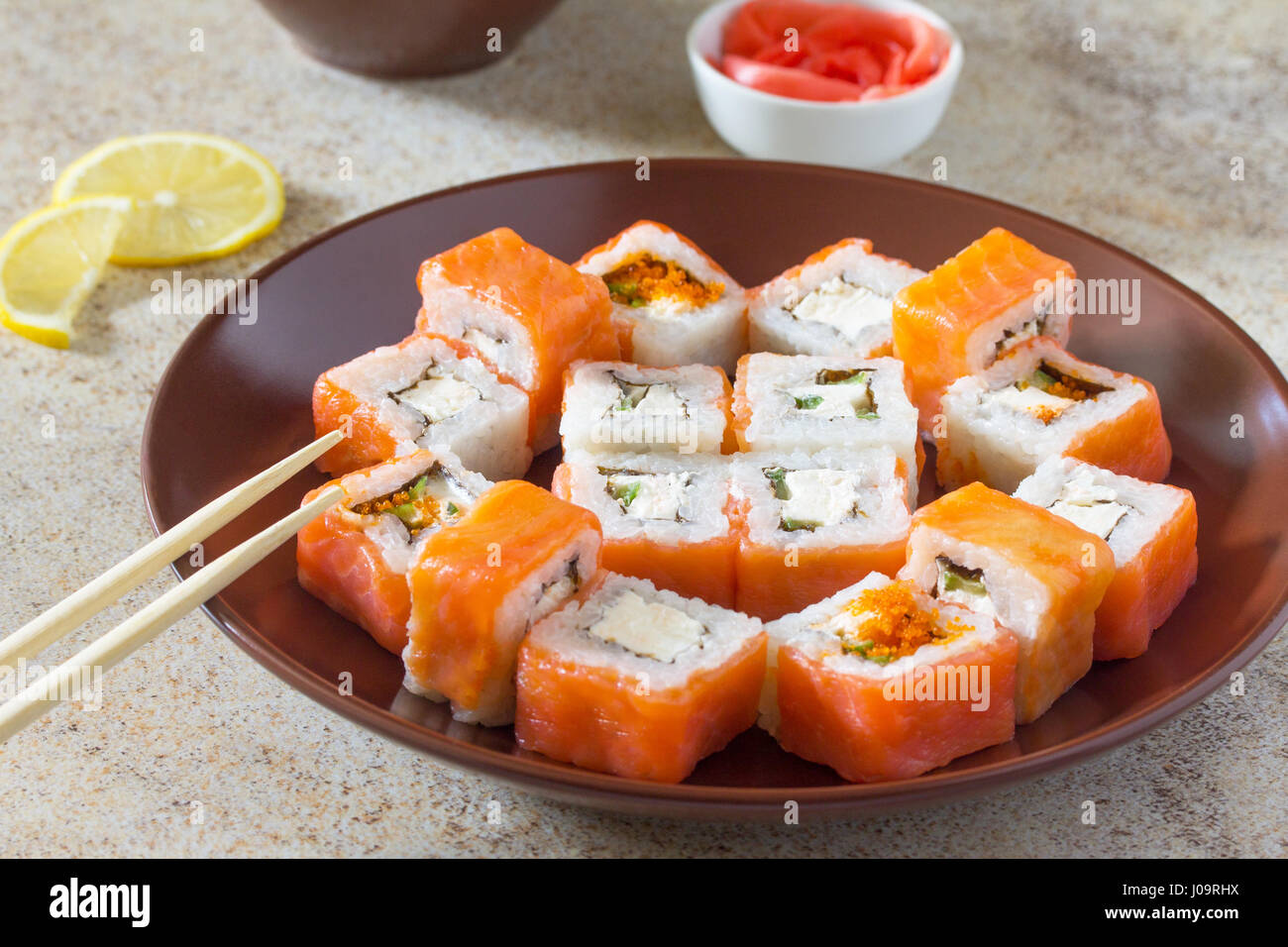 Sushi set on a stone background - roll Philadelphia classic, roll Cheese salmon and roll Jamaica with pickled ginger and soy sauce. Stock Photo