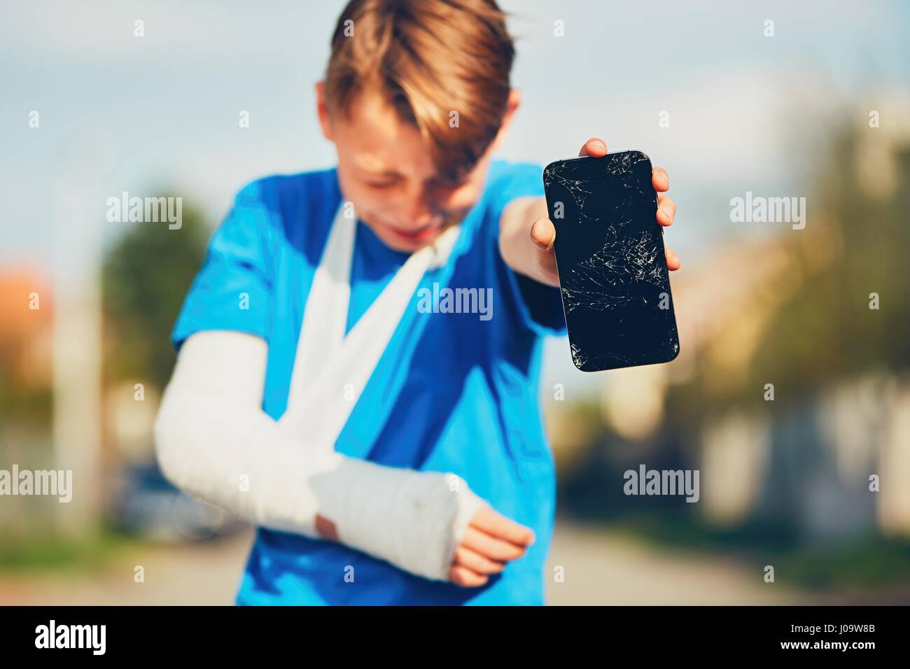 Little boy with broken hand injured after accident showing damaged mobile phone Stock Photo