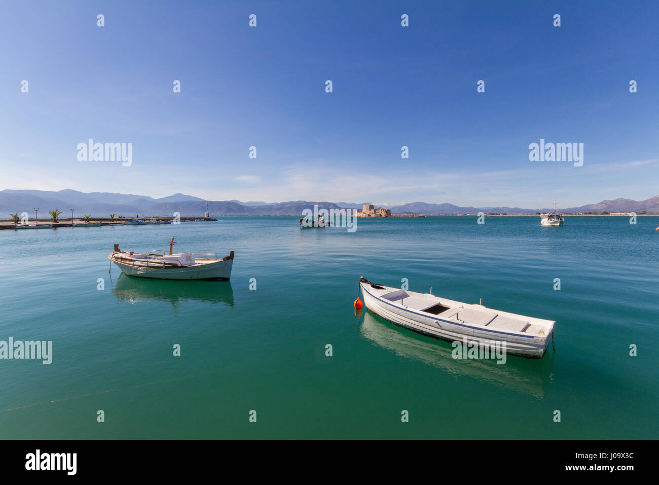 Moored Traditional Fishing Boats, Lightouse and Bourtzi Fortress in the background in Nafplion, Greece- wide-angle Stock Photo
