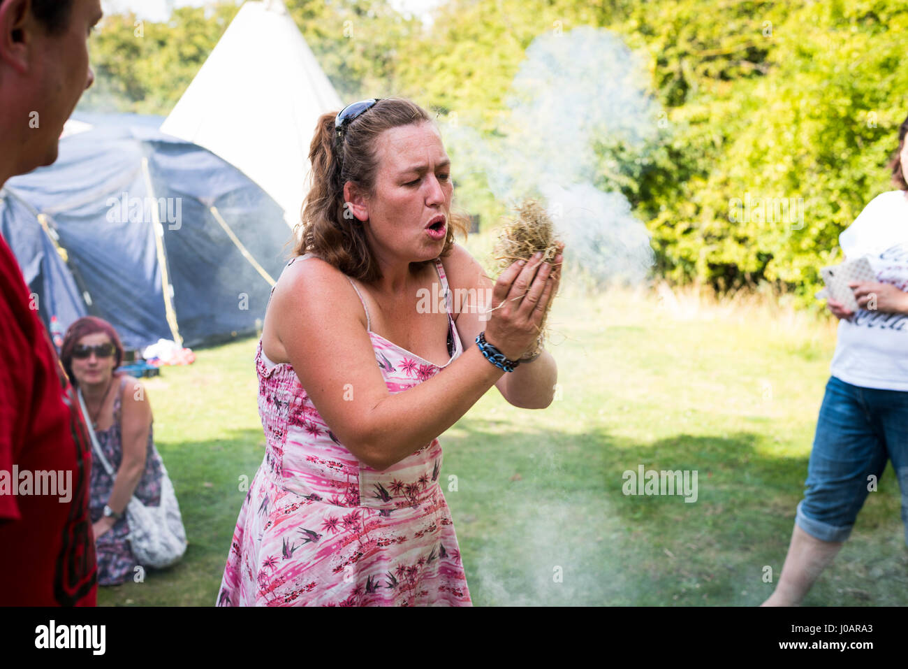 Woman blowing a small ember in a bundle of straw in a firelighting workshop at a festival Stock Photo