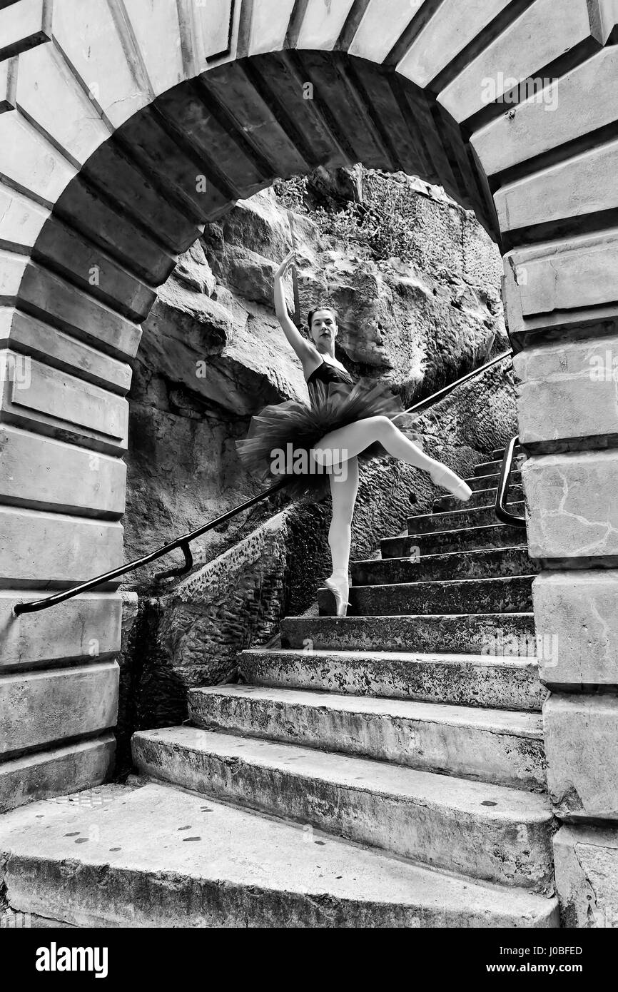 Young fit ballerina standing in ballet position at a bar on steps as part of street performance in The Rocks historic suburb of Sydney, Australia. Stock Photo
