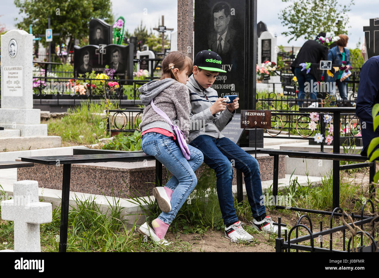 CHISINAU, MOLDOVA: A young boy plays on his mobile while his sister watches  the screen. VISITORS to Europe's largest graveyard have been snapped  breaking bread with the dead. What may seem morbid