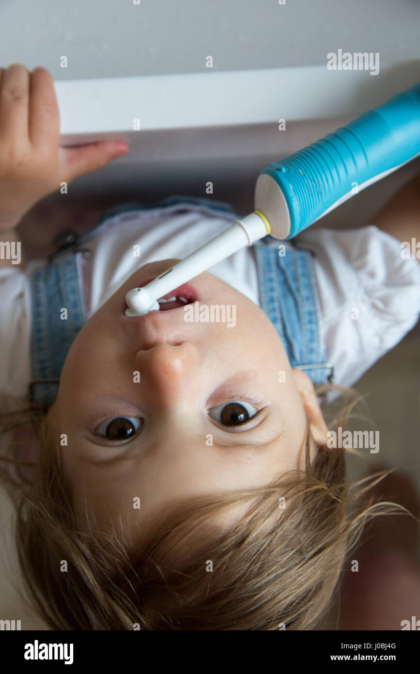 Girl toddler brushing her teeth using an adult electric toothbrush. She