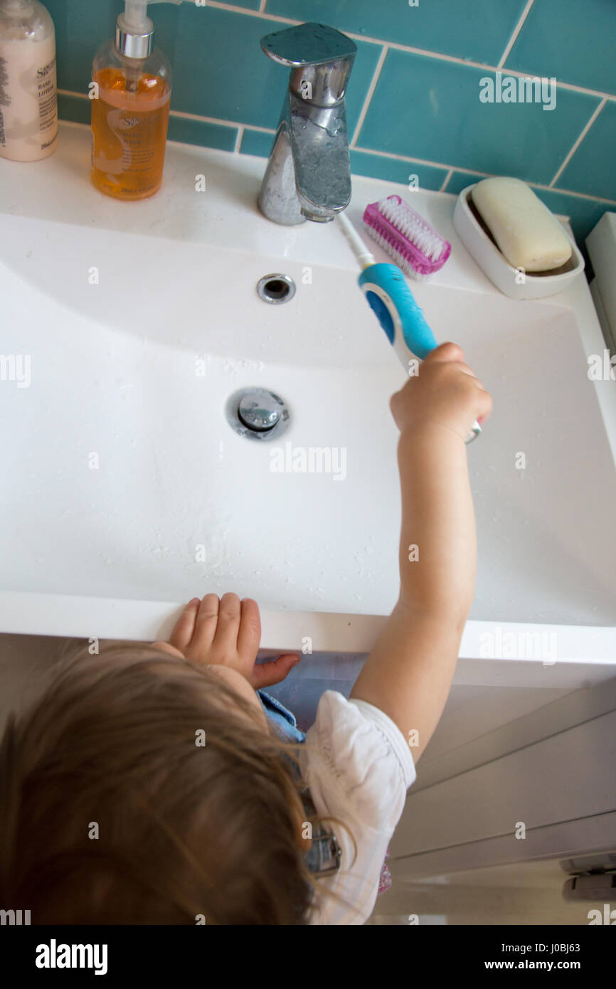 Girl toddler brushing her teeth using an adult electric toothbrush. She