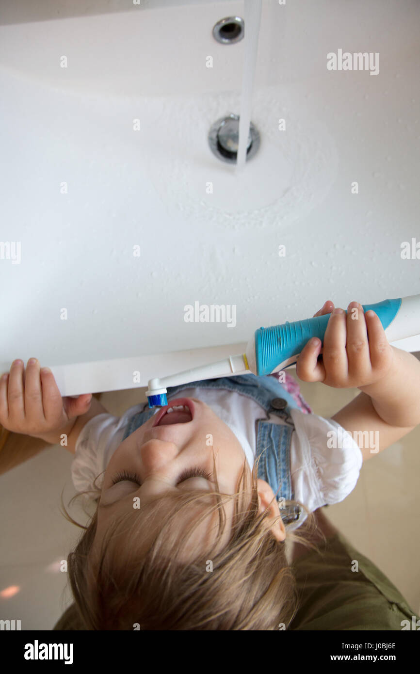 Girl toddler brushing her teeth using an adult electric toothbrush. She is 16 months old Stock Photo