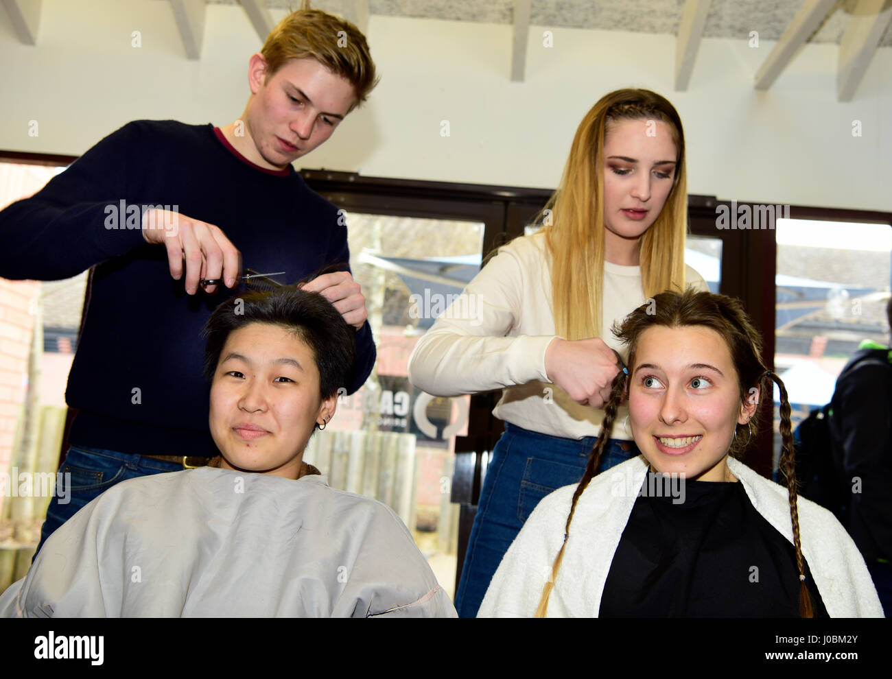 Two 18 year old college girls having their heads shaved by fellow students to help raise funds for Cancer Research, Alton, Hampshire, UK. 31.03.2017. Stock Photo