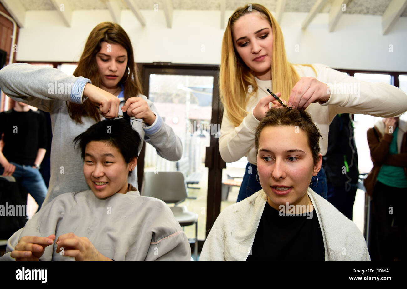 Two 18 year old college girls having their heads shaved by fellow students to help raise funds for Cancer Research, Alton, Hampshire, UK. 31.03.2017. Stock Photo