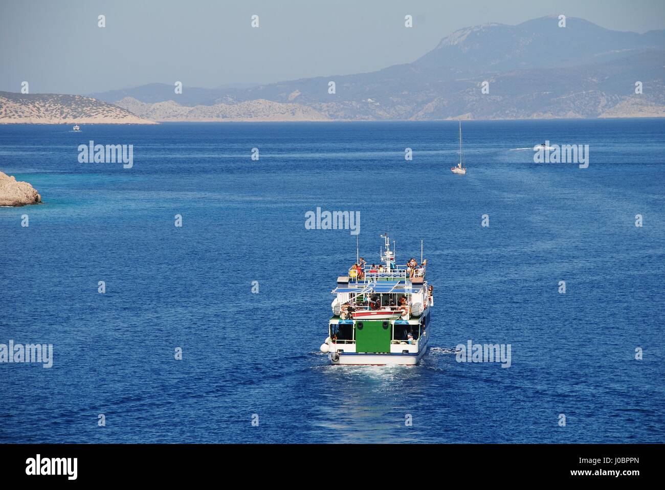 A ferry boat departs Emborio harbour on the Greek island of Halki. Stock Photo