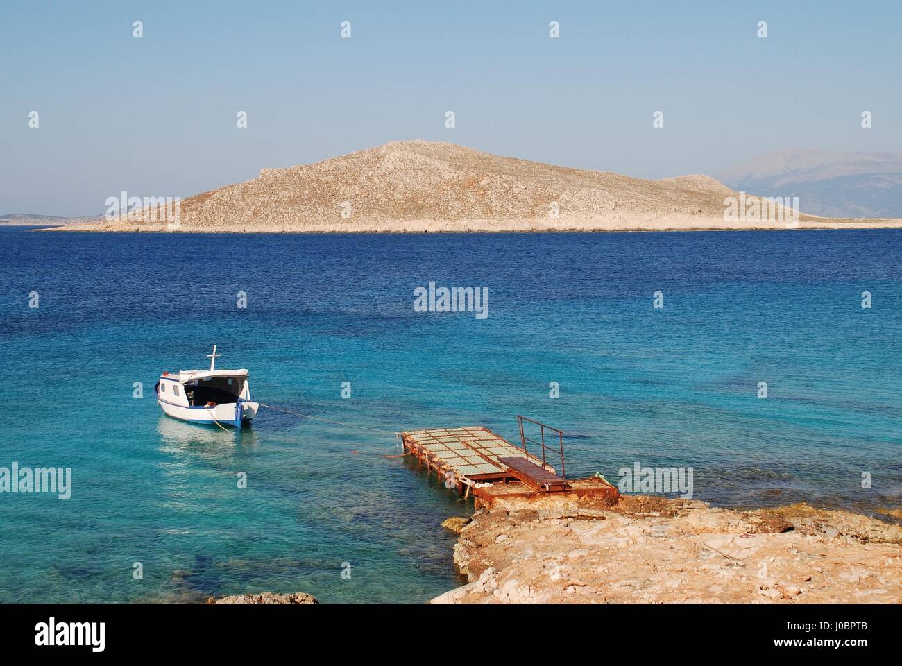 A small boat moored by Ftenagia beach at Emborio on the Greek island of Halki. The uninhabited island of Nissos is in the background. Stock Photo