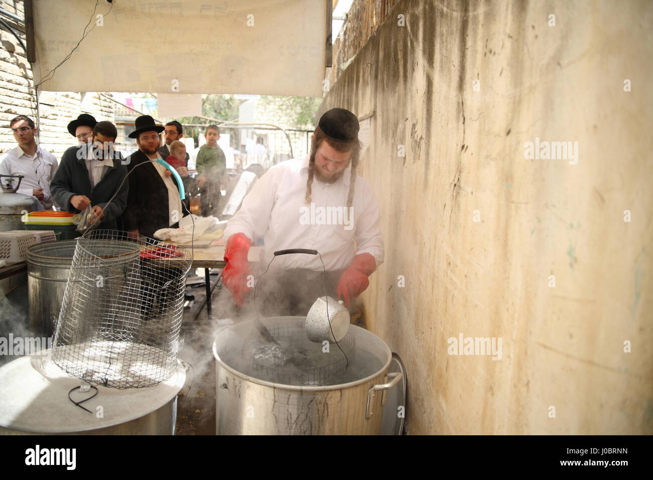 An Orthodox Jewish man gets paid by customers for immersing dishes in boiling water in huge pots to make them Kosher for the upcoming Passover Holiday Stock Photo