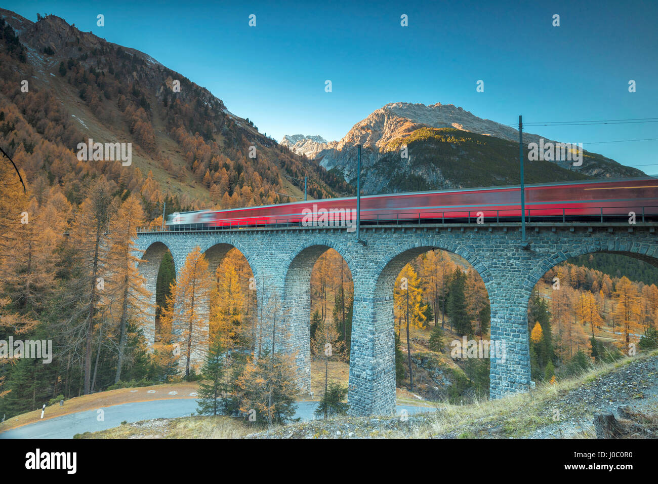Red train on viaduct surrounded by colorful woods, Preda, Bergun, Albula Valley, Canton of Graubunden, Engadine, Switzerland Stock Photo