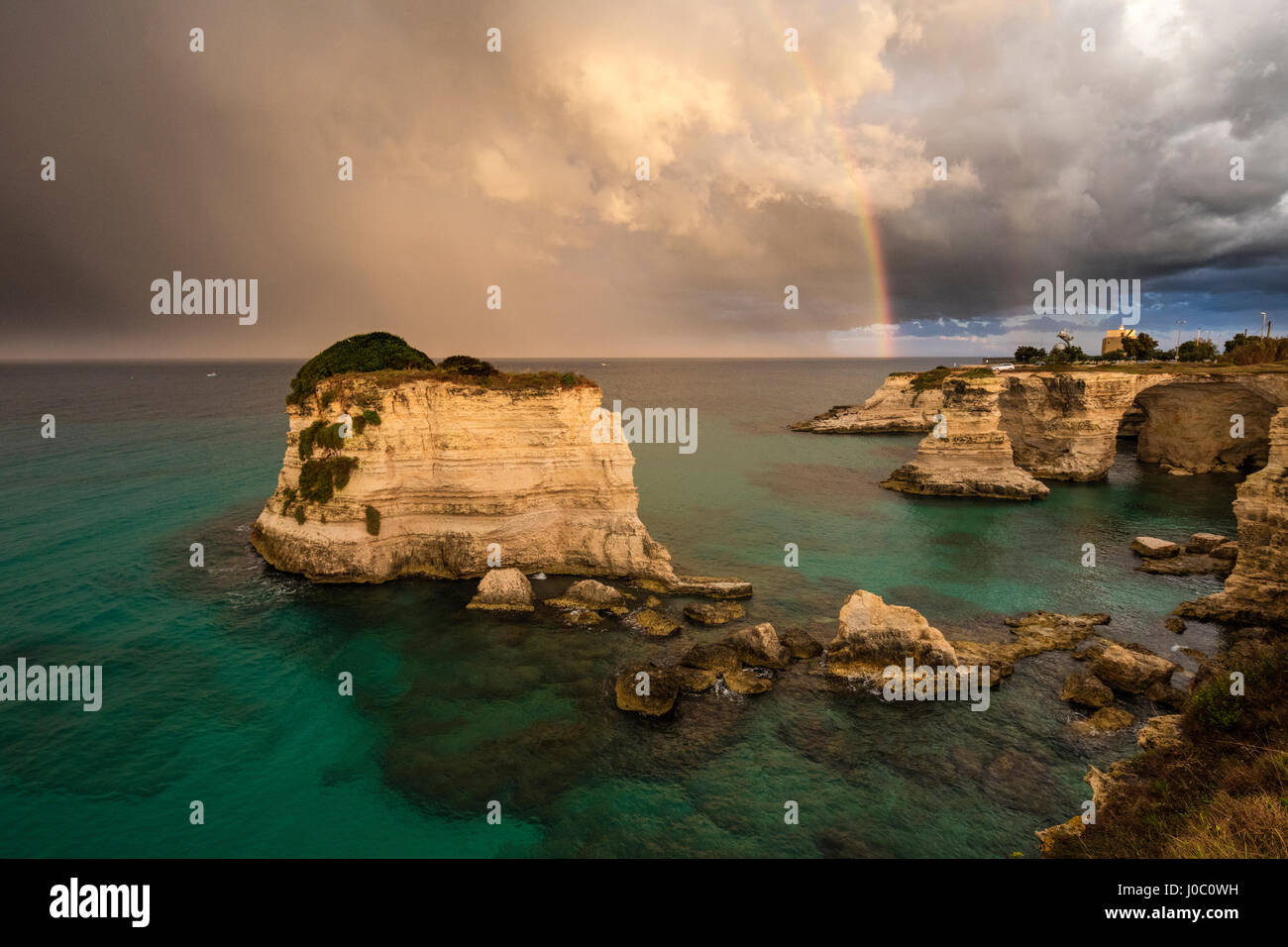 Rainbow frames rocky cliffs known as Faraglioni di Sant'andrea surrounded by turquoise sea, province of Lecce, Apulia, Italy Stock Photo