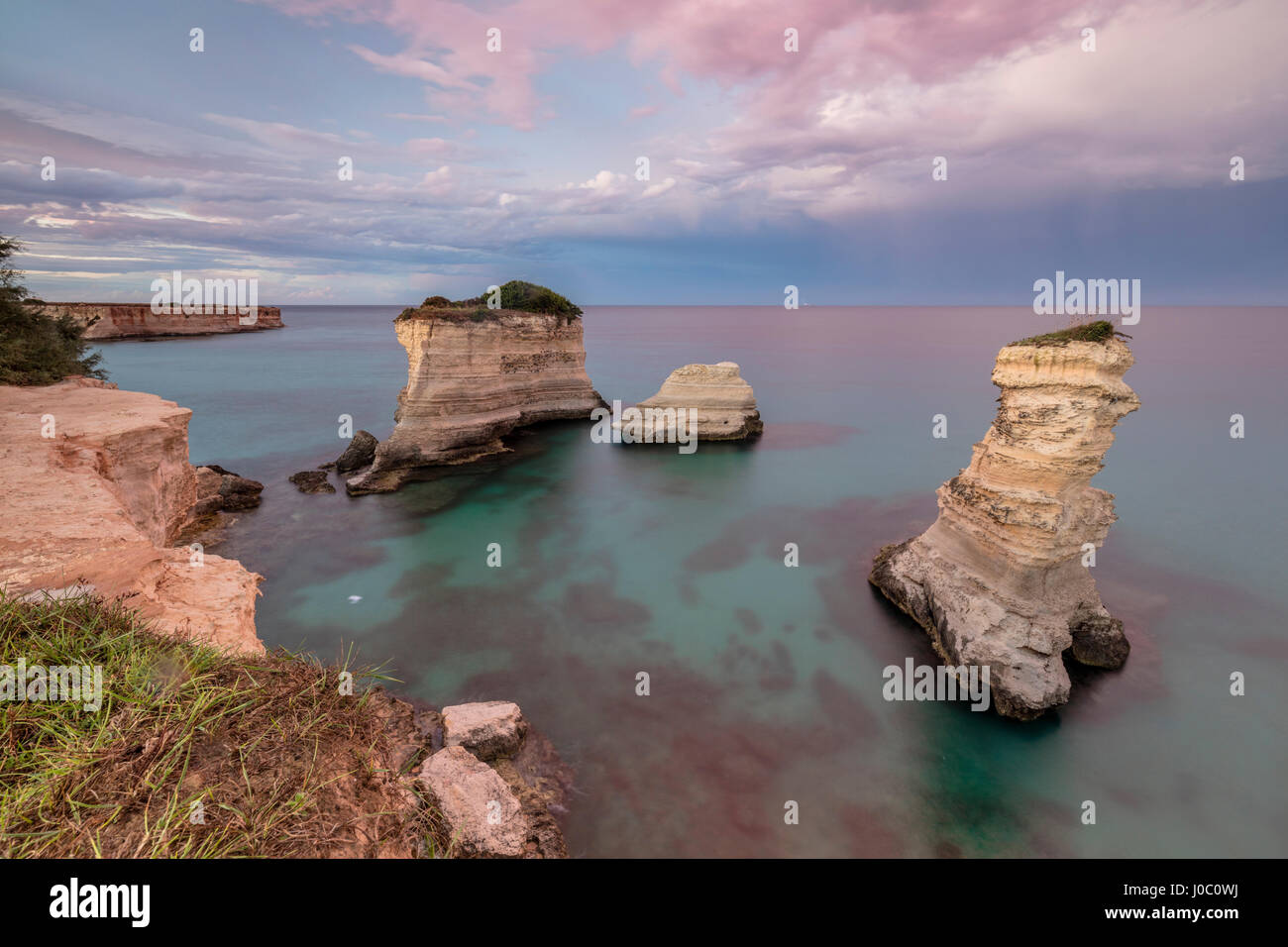 Pink sunset frames the cliffs known as Faraglioni di Sant&rsquo;Andrea and
