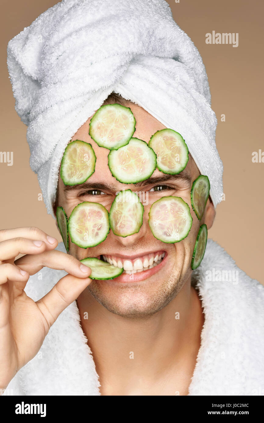 Funny man receiving facial mask of cucumber. Cosmetic procedure man's face. Grooming himself Stock Photo