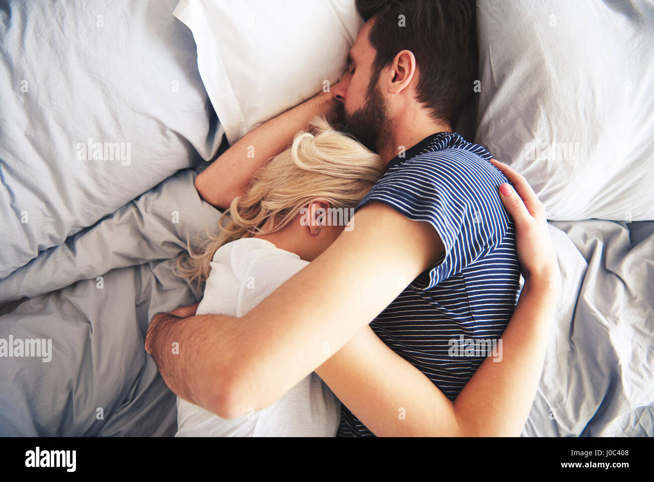 Couple lying in bed together, sleeping, arms around each other Stock Photo