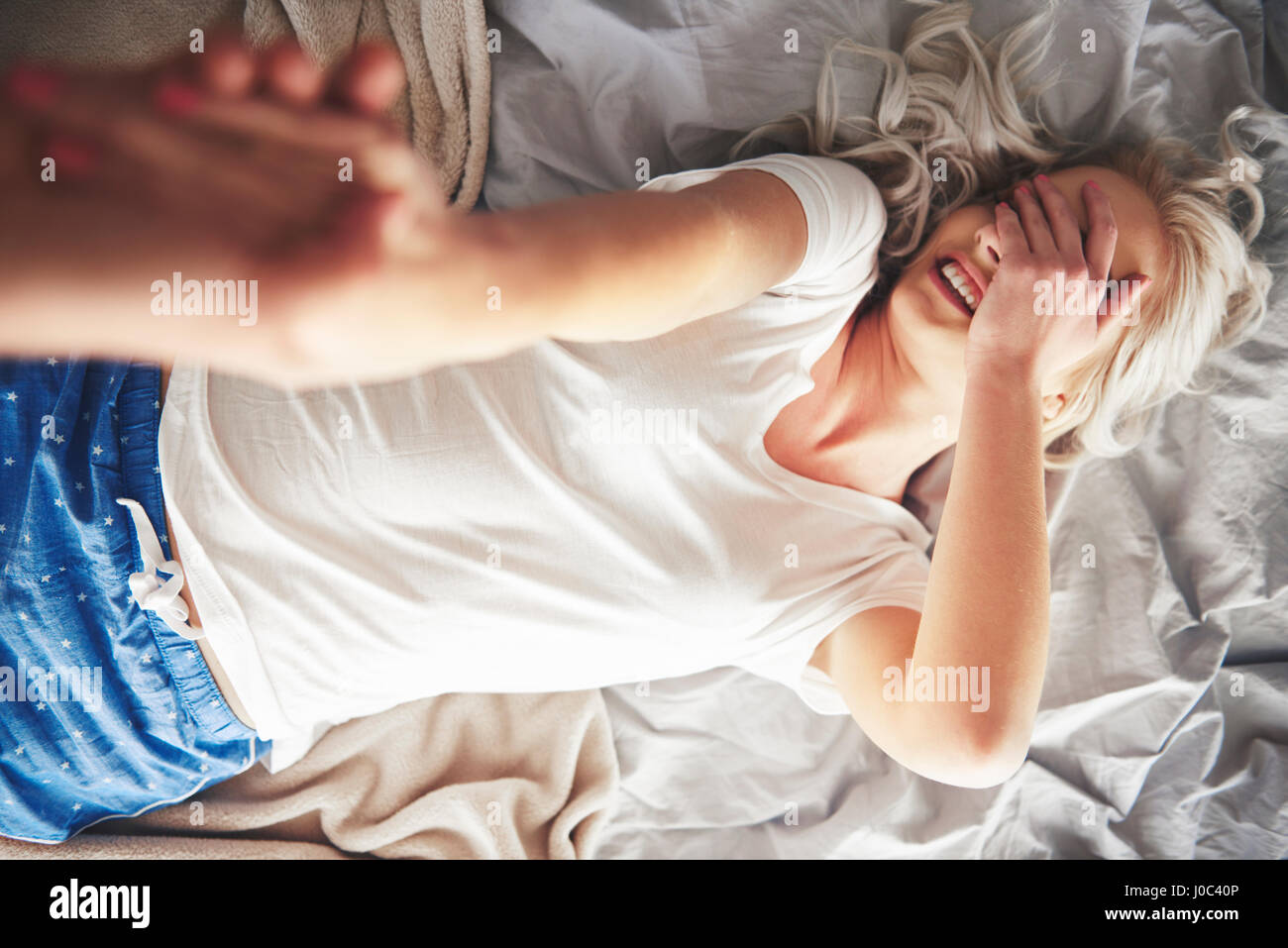 Woman lying on bed, man pulling her off bed, elevated view Stock Photo