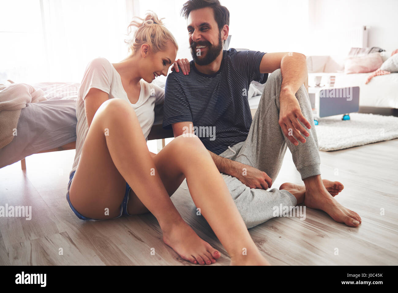 Couple sitting on floor beside bed, laughing Stock Photo