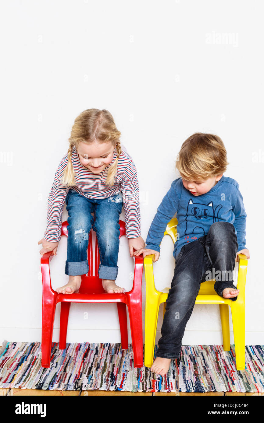 Young boy and girl , crouching on colourful chairs Stock Photo