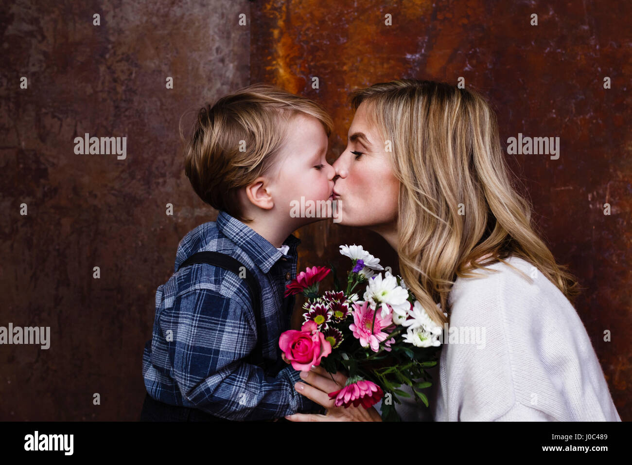 Young boy giving bunch of flowers to mother, mother kissing boy Stock Photo