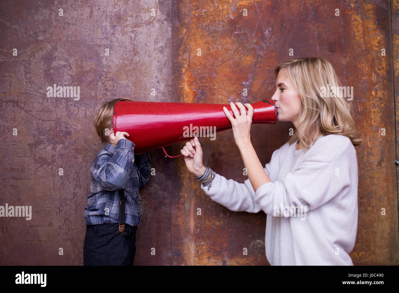 Woman speaking into megaphone, young boy listening, head in megaphone Stock Photo