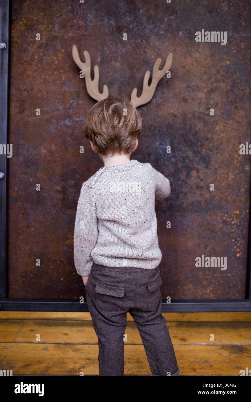 Young boy standing facing wall, cardboard reindeer cut out on wall behind him Stock Photo