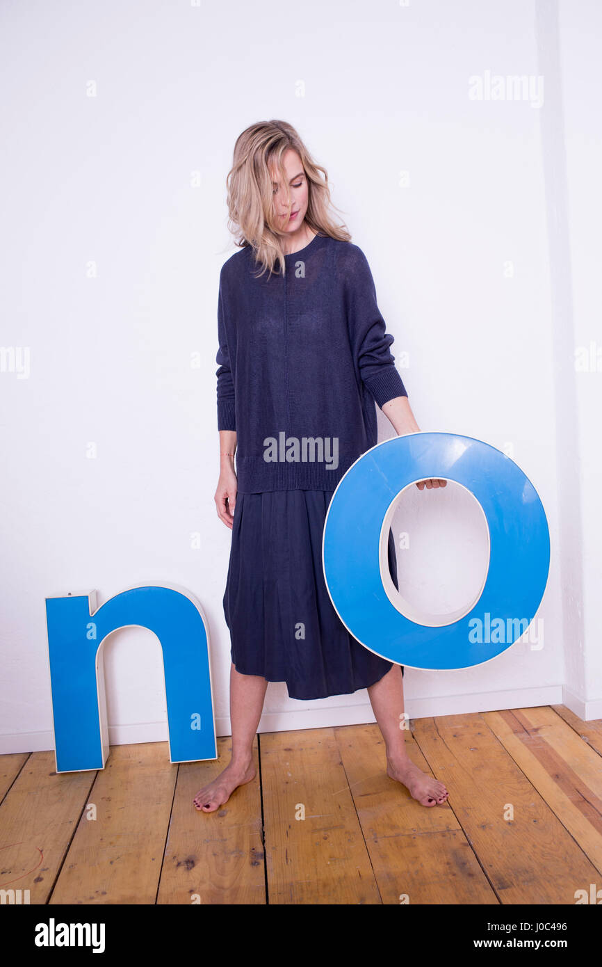 Portrait of mid adult woman, holding three-dimensional letter 'O', next to letter 'N' on floor Stock Photo