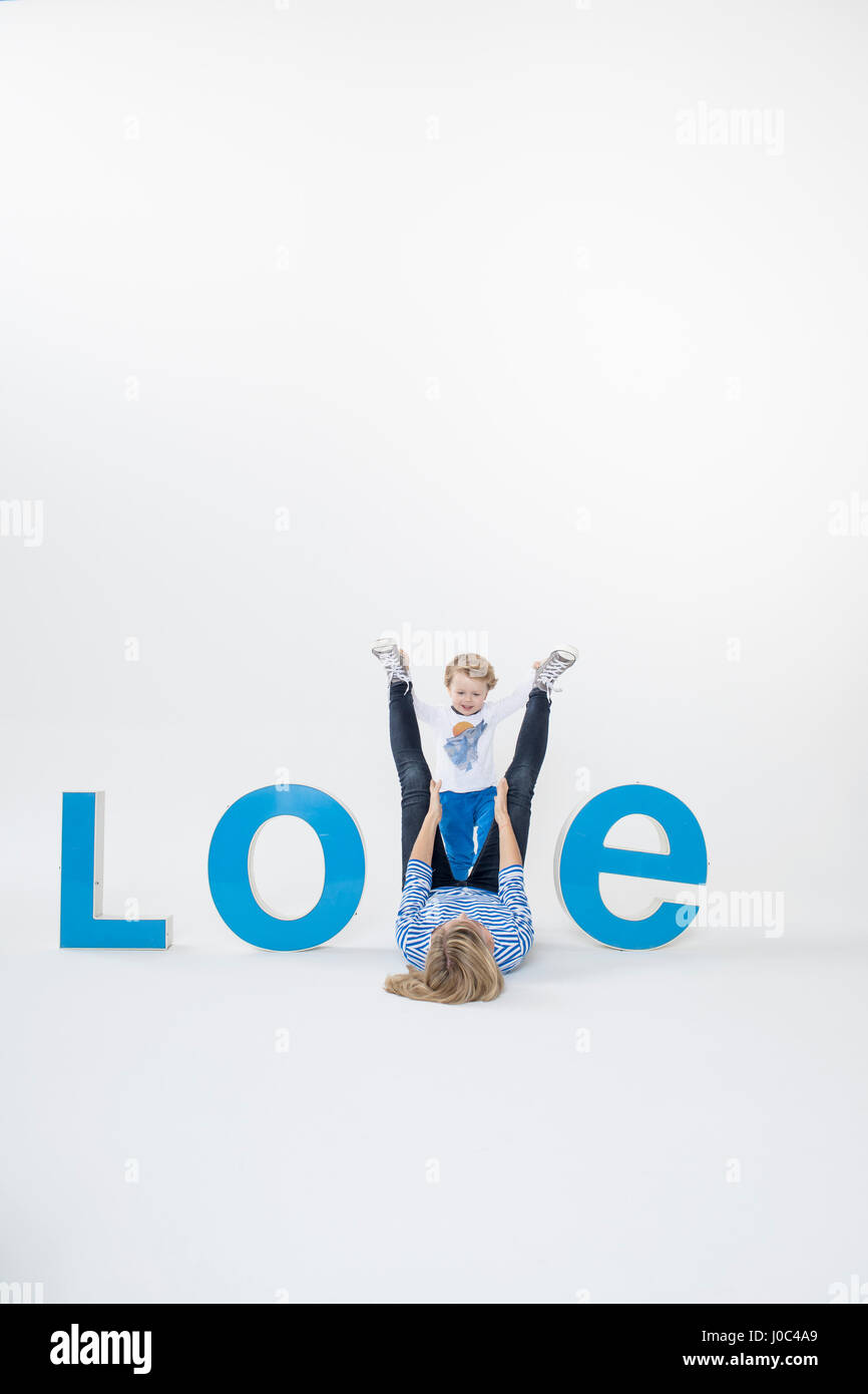 Mother and son lying on floor between three-dimensional letters, creating the word LOVE Stock Photo
