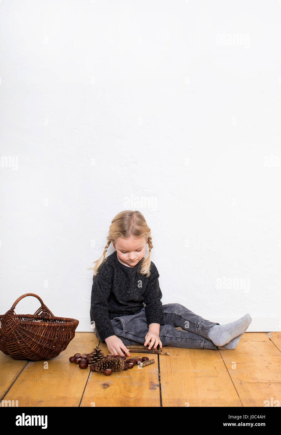 Young girl sitting on floor, sorting through pine cones and conkers Stock Photo