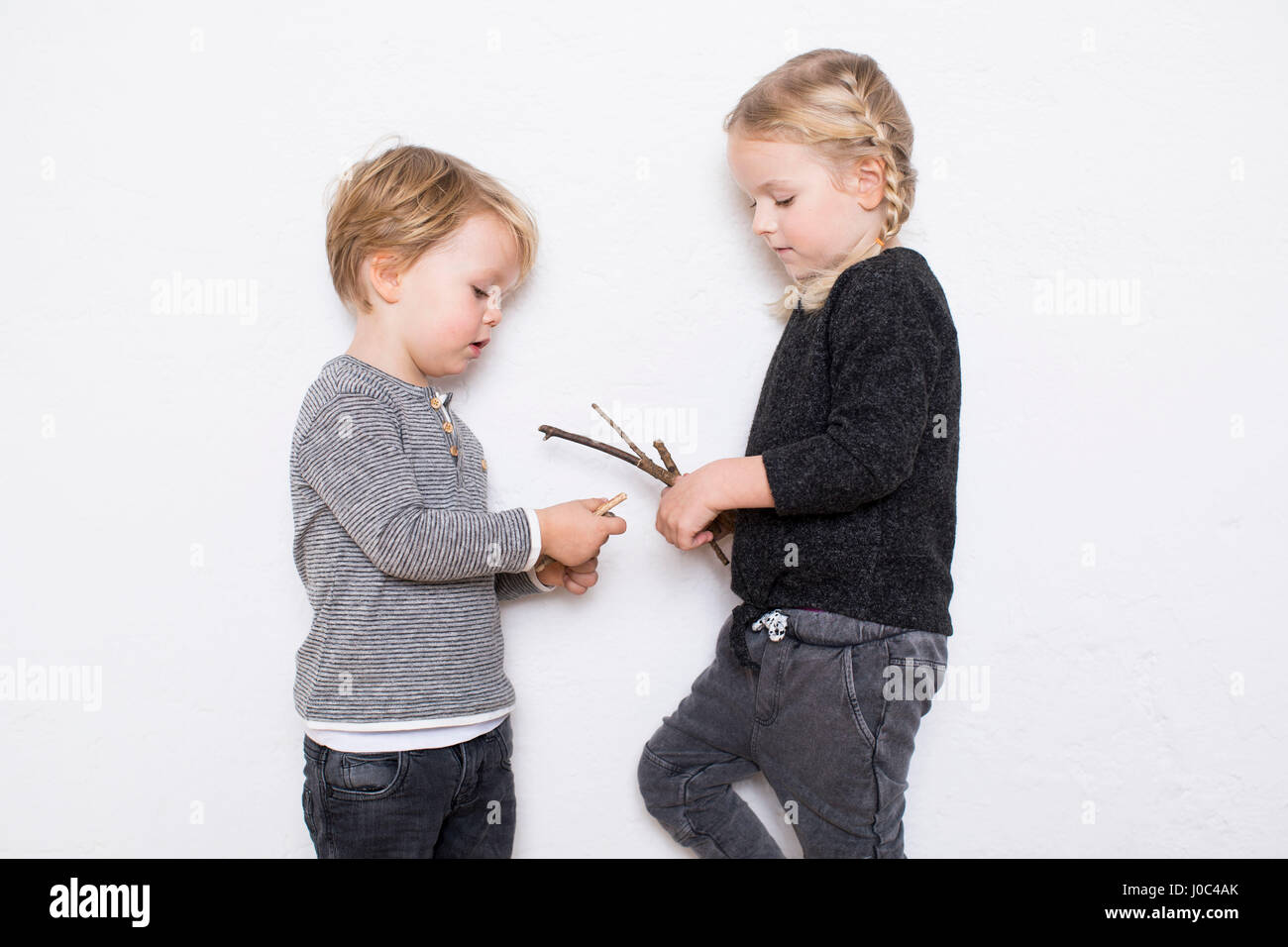 Young girl and boy leaning against white background, girl holding twigs Stock Photo