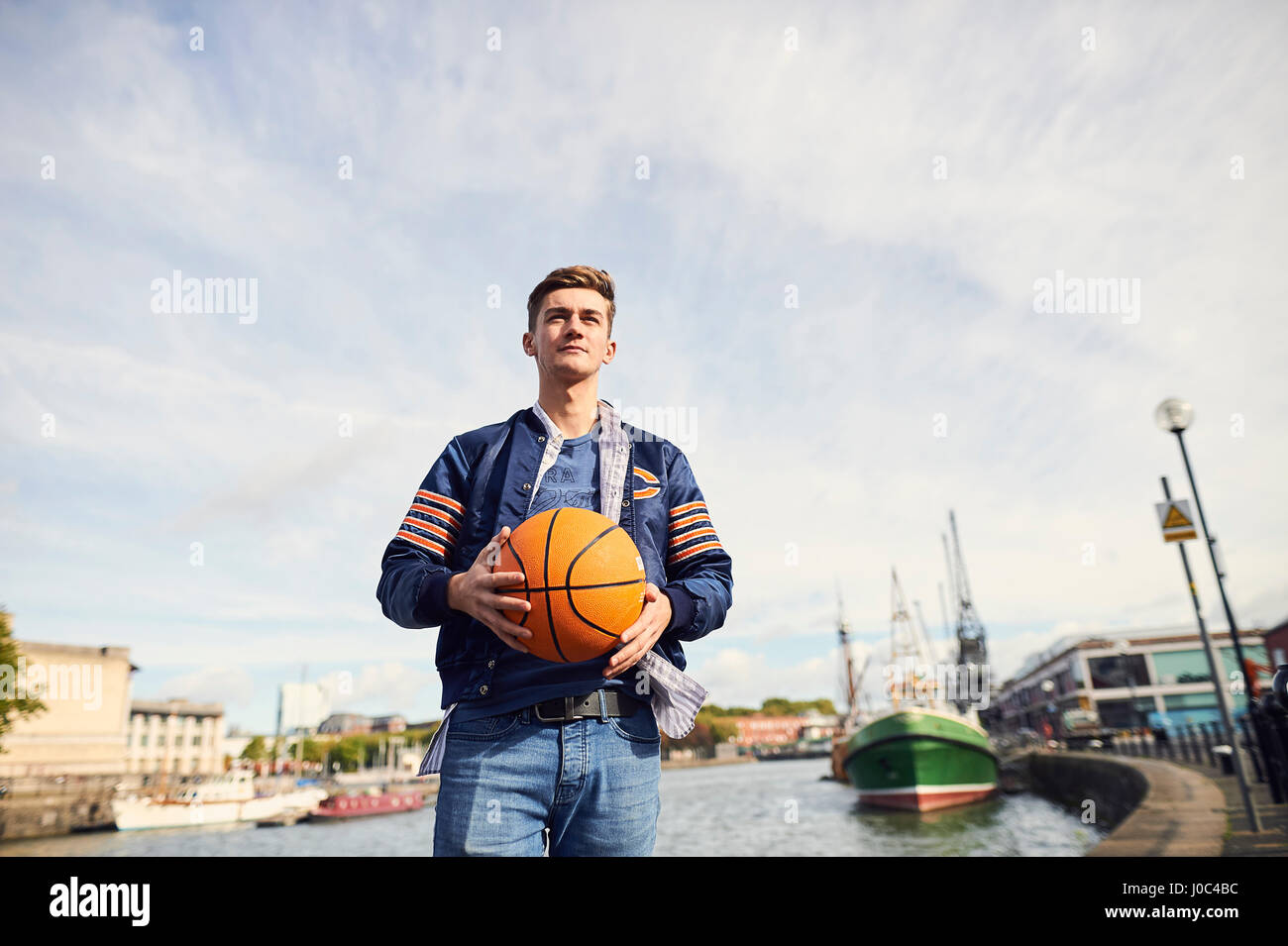 Young man near river, holding basketball, Bristol, UK Stock Photo