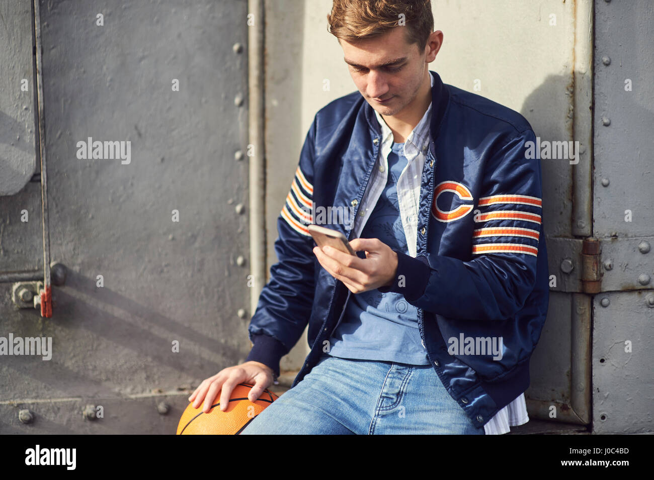 Young man sitting outdoors, using smartphone, holding basketball, Bristol, UK Stock Photo
