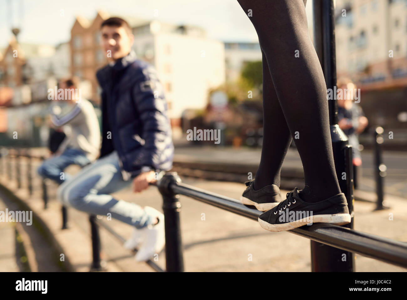 Young man sitting on railing, young girl walking along railing next to him, Bristol, UK Stock Photo