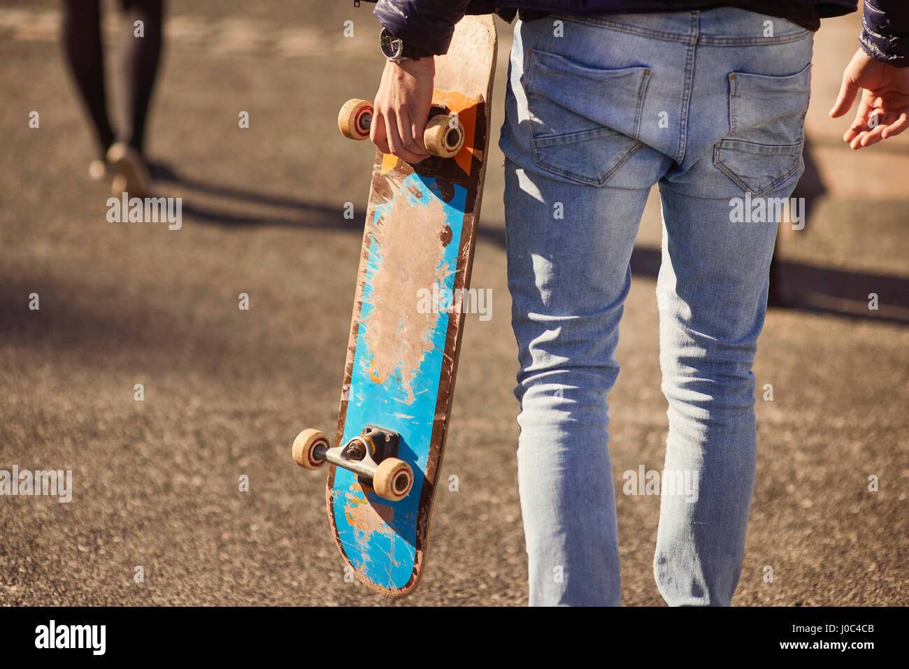 Young man walking outdoors, carrying skateboard, rear view, low section, Bristol, UK Stock Photo