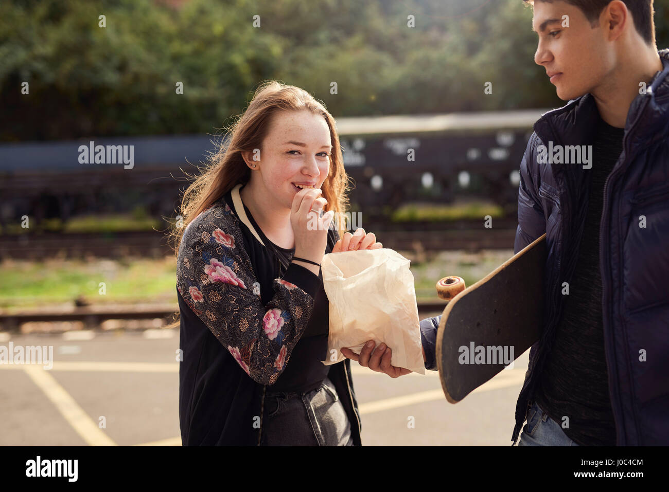 Young man sharing bag of chips with young woman,  skateboard under young man's arm, Bristol, UK Stock Photo