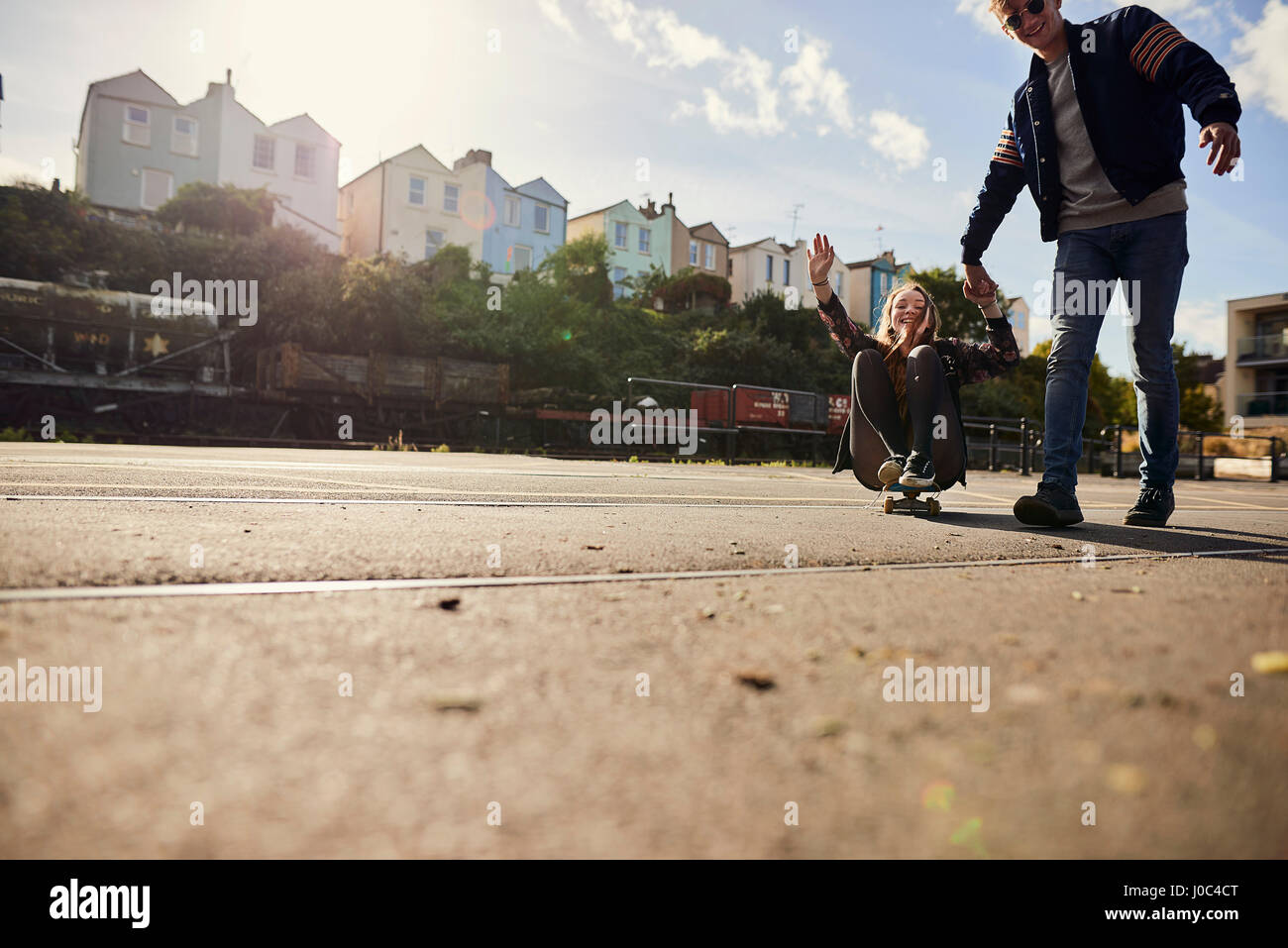 Two friends fooling around, young man pulling young woman along on skateboard, Bristol, UK Stock Photo