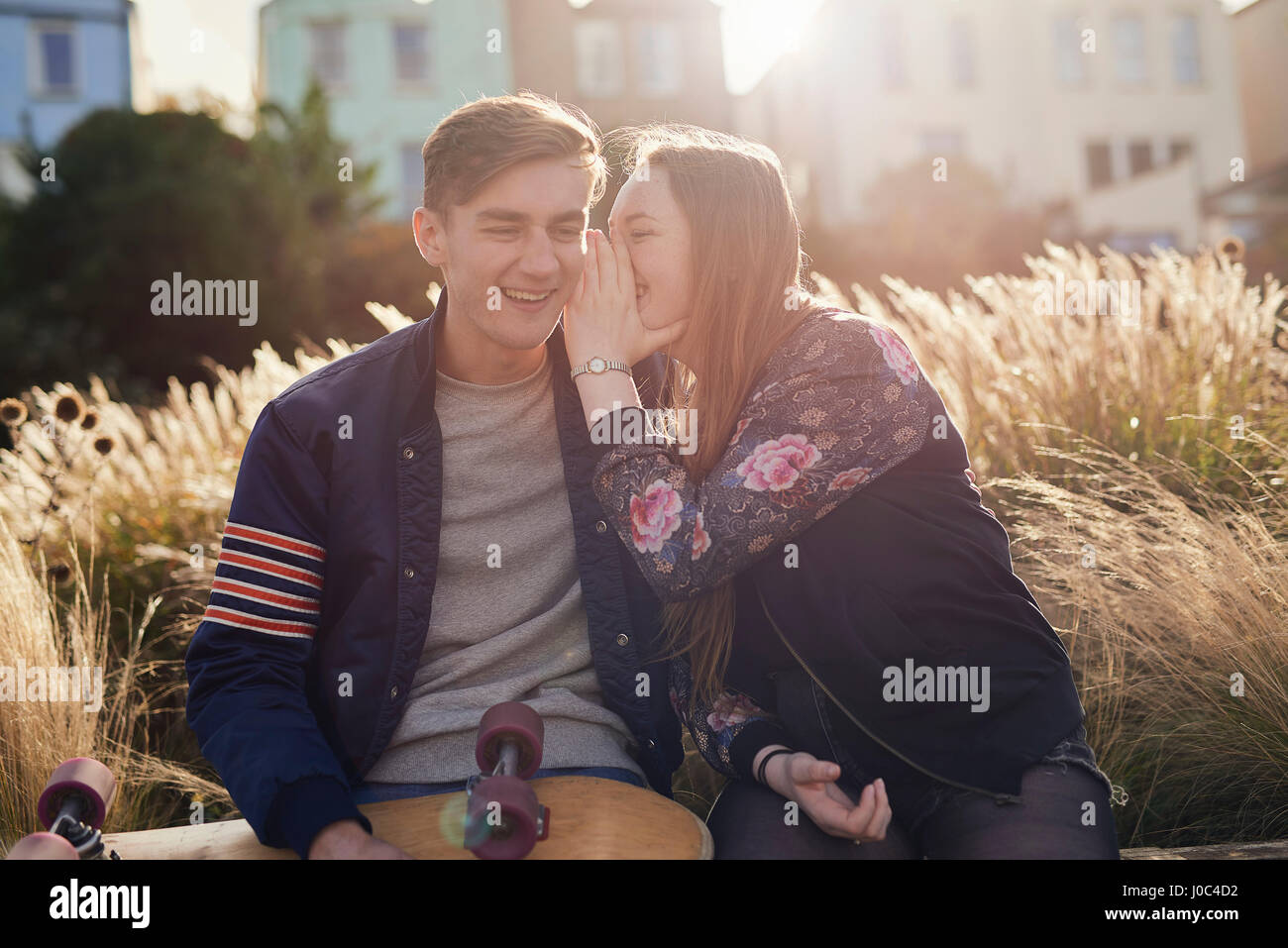 Two friends sitting outdoors, young woman whispering to young man, Bristol, UK Stock Photo