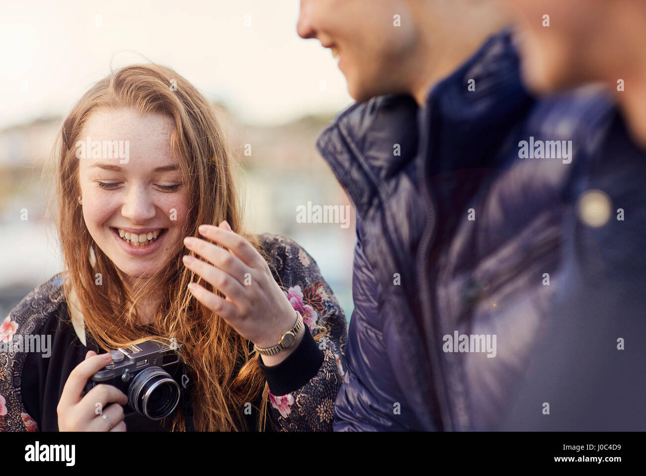 Three friends outdoors, young woman holding camera, laughing, Bristol, UK Stock Photo