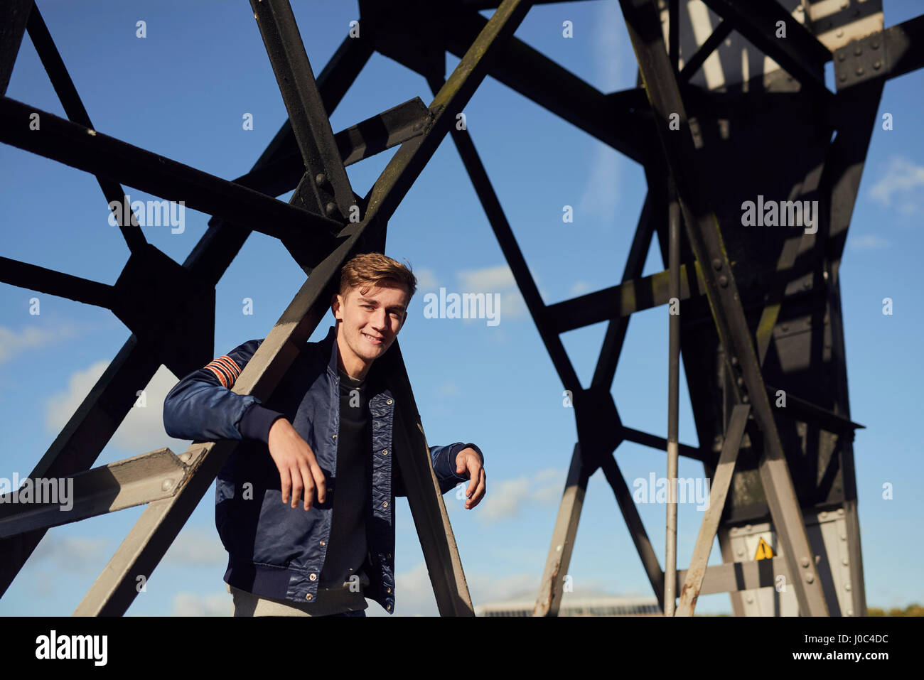 Portrait of young man, arms hooked around metal structure, Bristol, UK Stock Photo