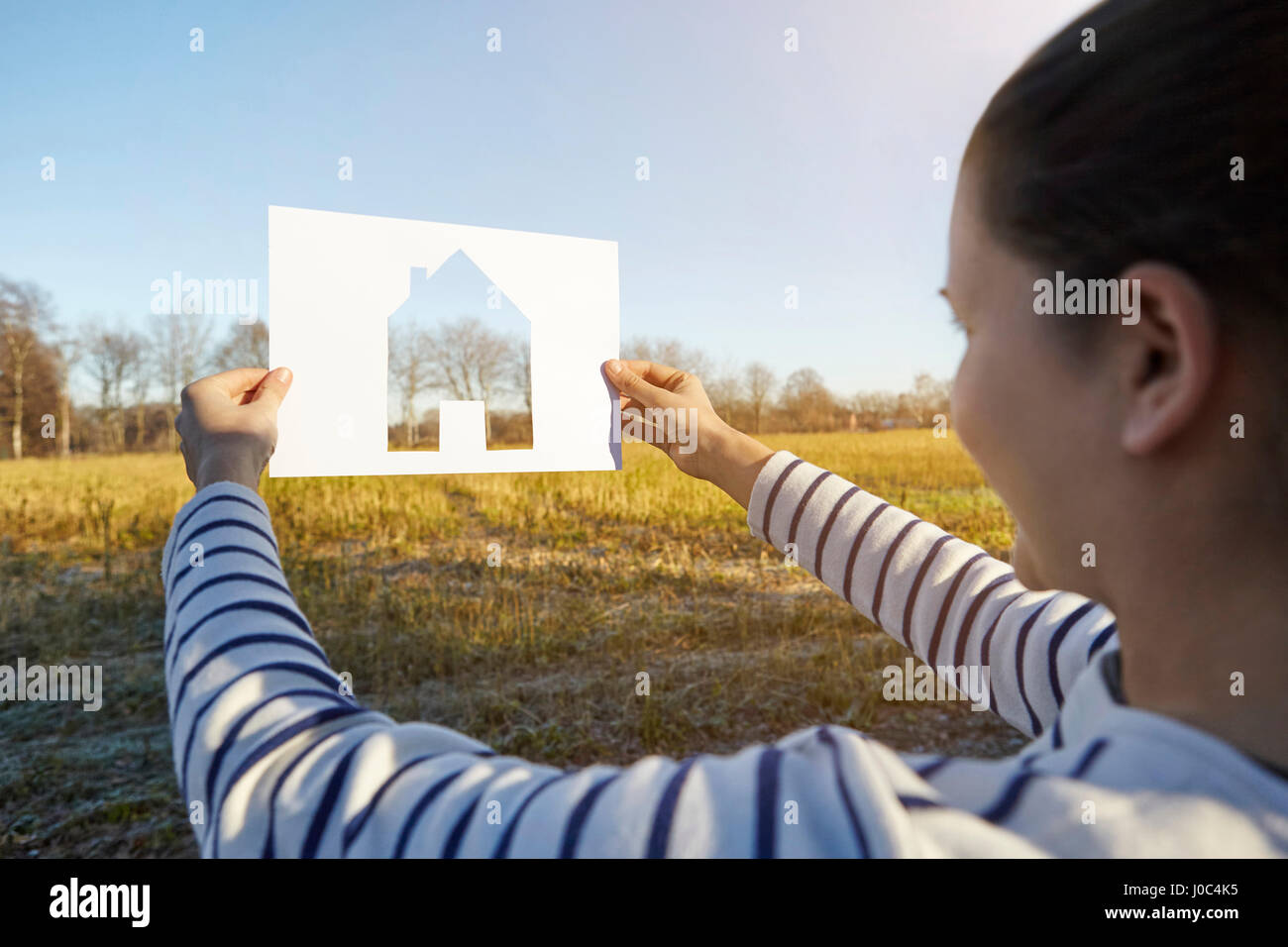 Woman standing in rural setting, holding out paper with cut-out of house Stock Photo