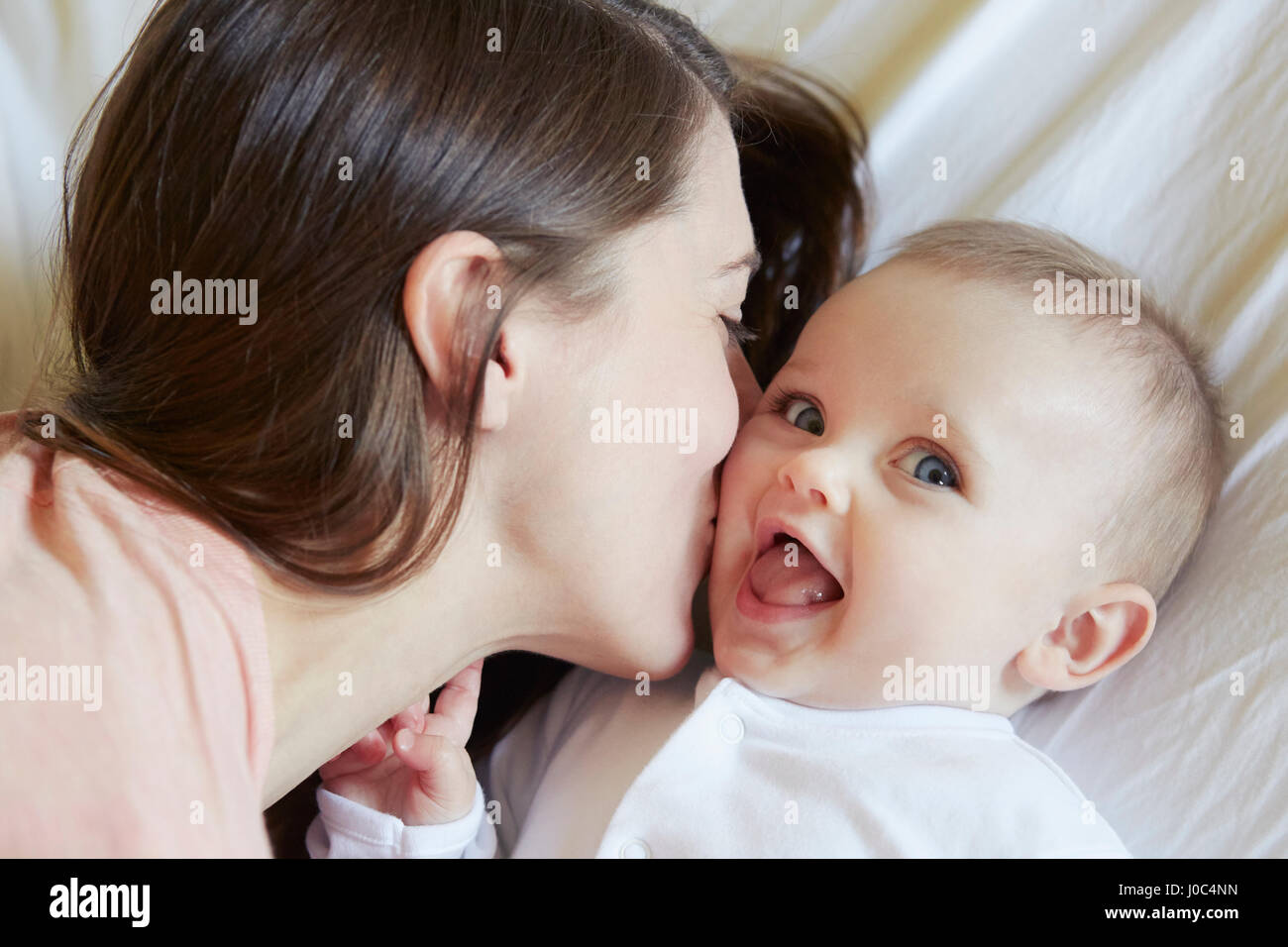 Portrait of cute baby girl being kissed by mother on bed Stock Photo