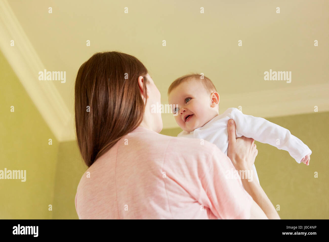 Low angle view of mid adult woman holding baby daughter in bedroom Stock Photo