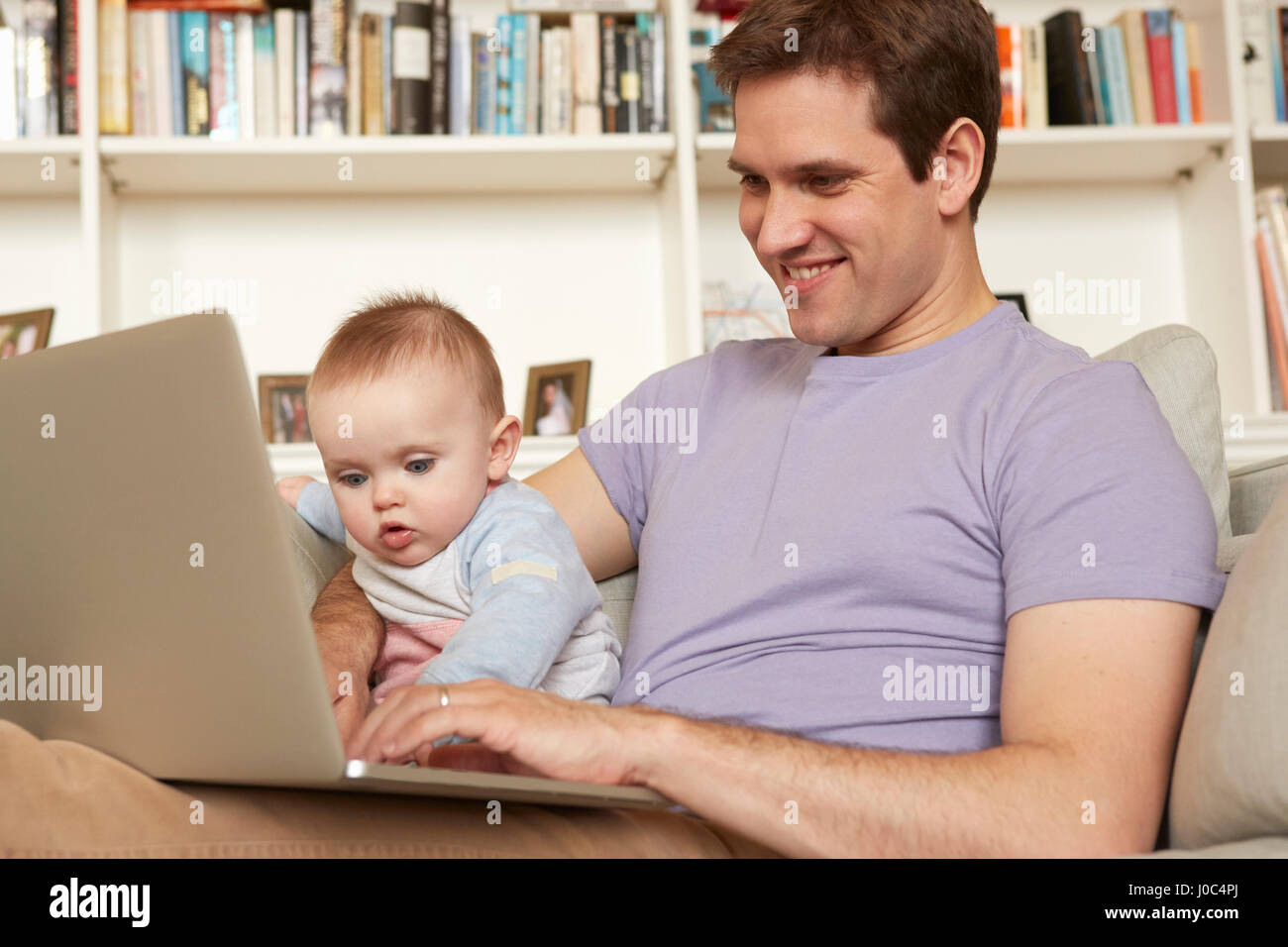 Baby girl helping father with laptop typing on sofa Stock Photo