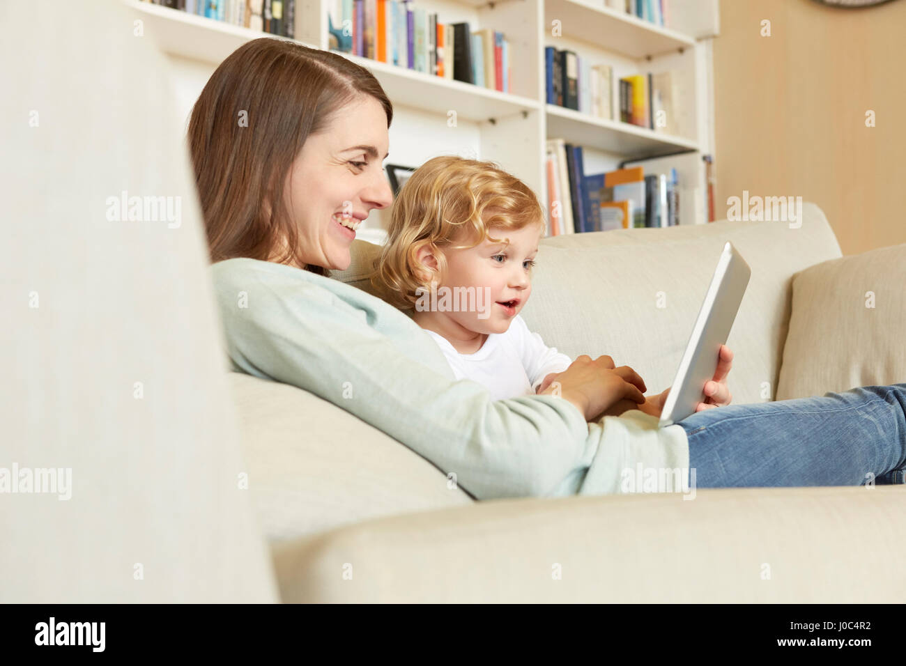 Female toddler sitting on sofa with mother looking at digital tablet Stock Photo
