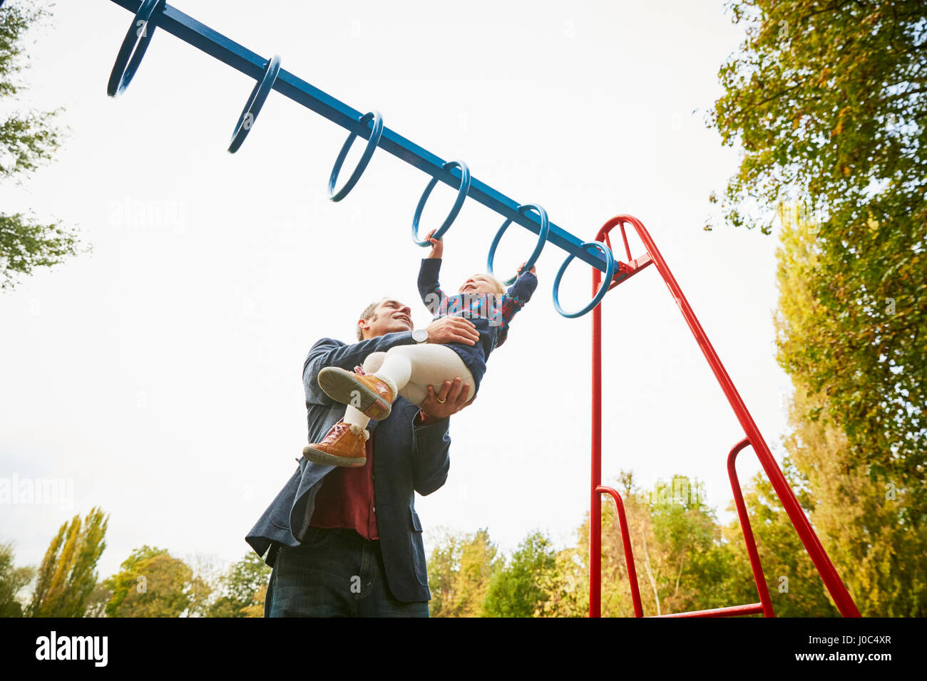 Father helping daughter on monkey bars in playground Stock Photo