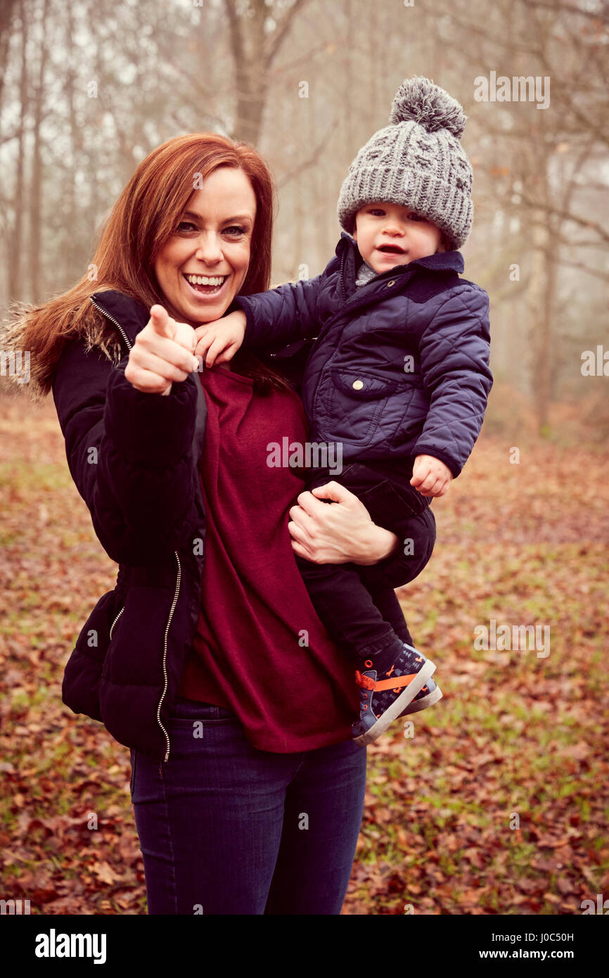 Mid adult woman carrying toddler son and pointing in autumn forest